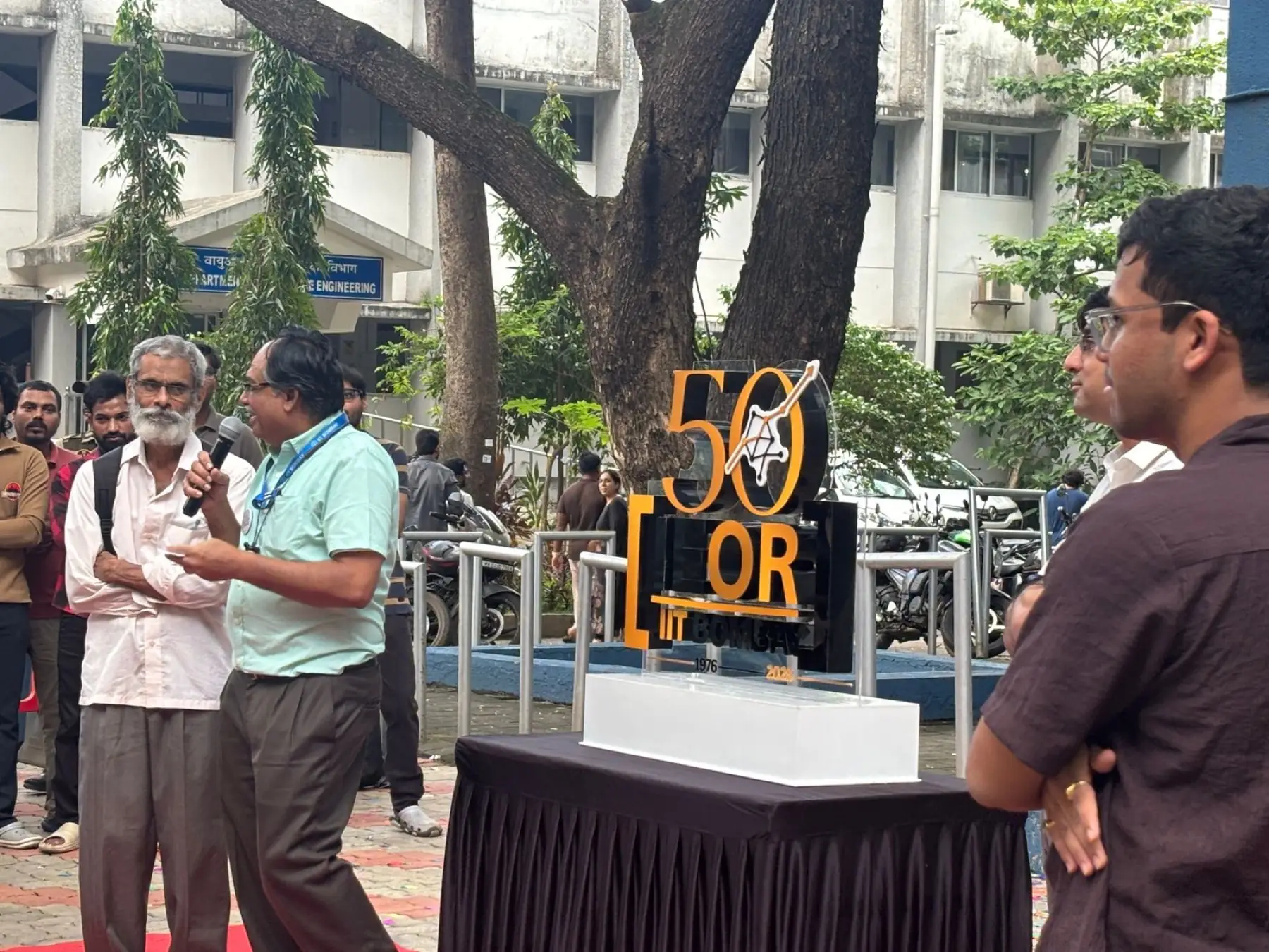 Two faculty members beside the Golden Jubilee mark under a tree