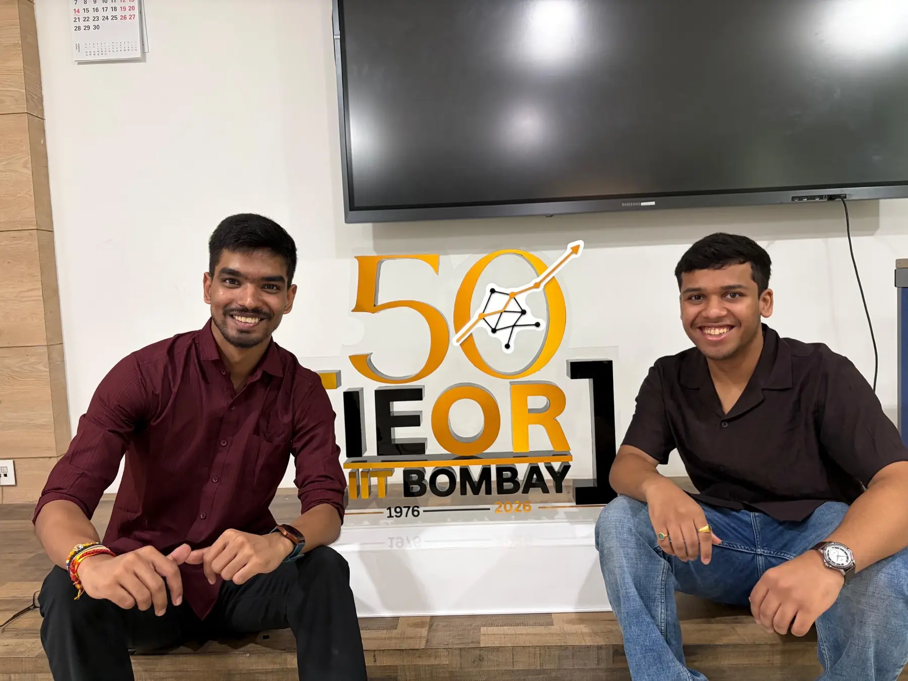 Two students seated indoors with the Golden Jubilee mark between them